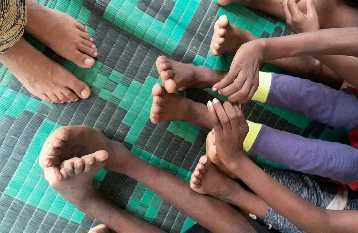 Pies descalzos de niños y adultos sobre una estera verde, vistos desde arriba