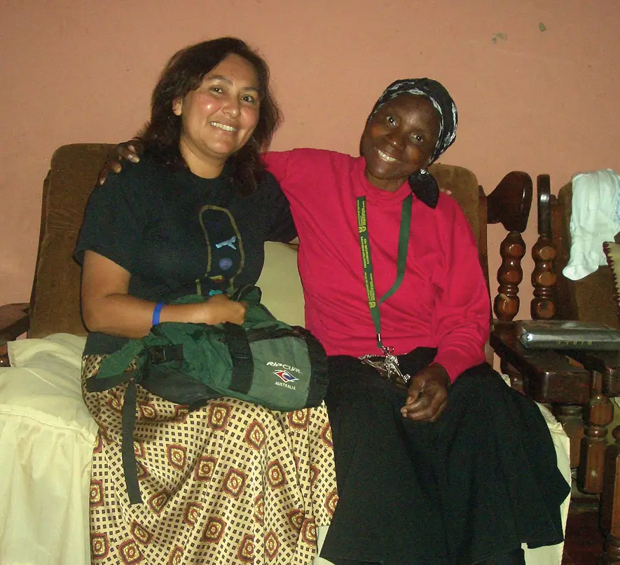 Una obrera de SIM y una mujer de la comunidad, sentadas juntas y sonriendo en la casa de ella